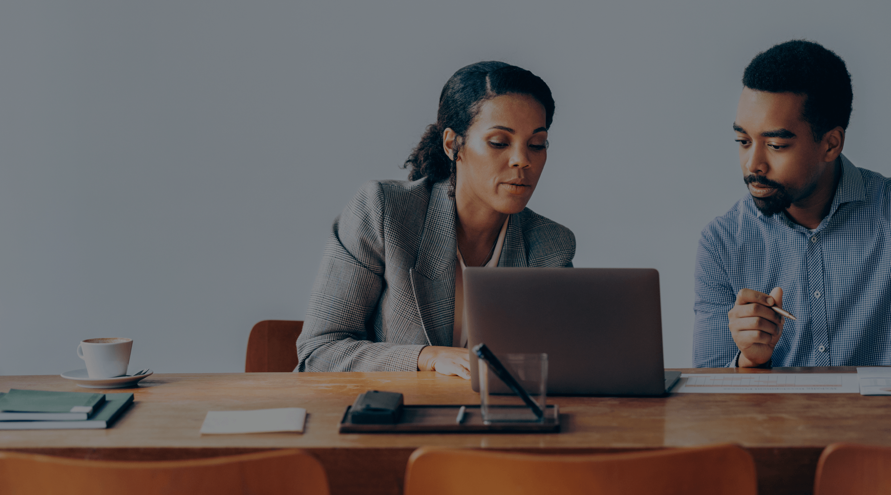 Image of two people working at a laptop at a table.